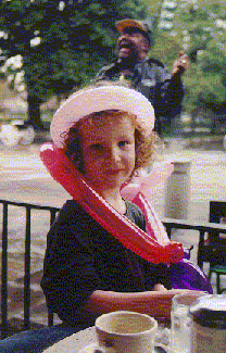 Balloon bedecked Maggie eating beignet at the Cafe du Monde in New Orleans, while a street performer sings